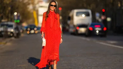 Alba Garavito Torre wears black sunglasses from Ray Ban, gold fringed metallic pendant earrings, a red with beige polka dots print pattern knot high neck / puffy sleeves / ruffled long dress from Zimmermann, gold bracelets, gold rings, a beige matte leather handbag from Jacquemus, gold shiny leather knot toe-cap block heels mules / sandals from What For, during a street style fashion photo session, on March 23, 2022 in Paris, France.