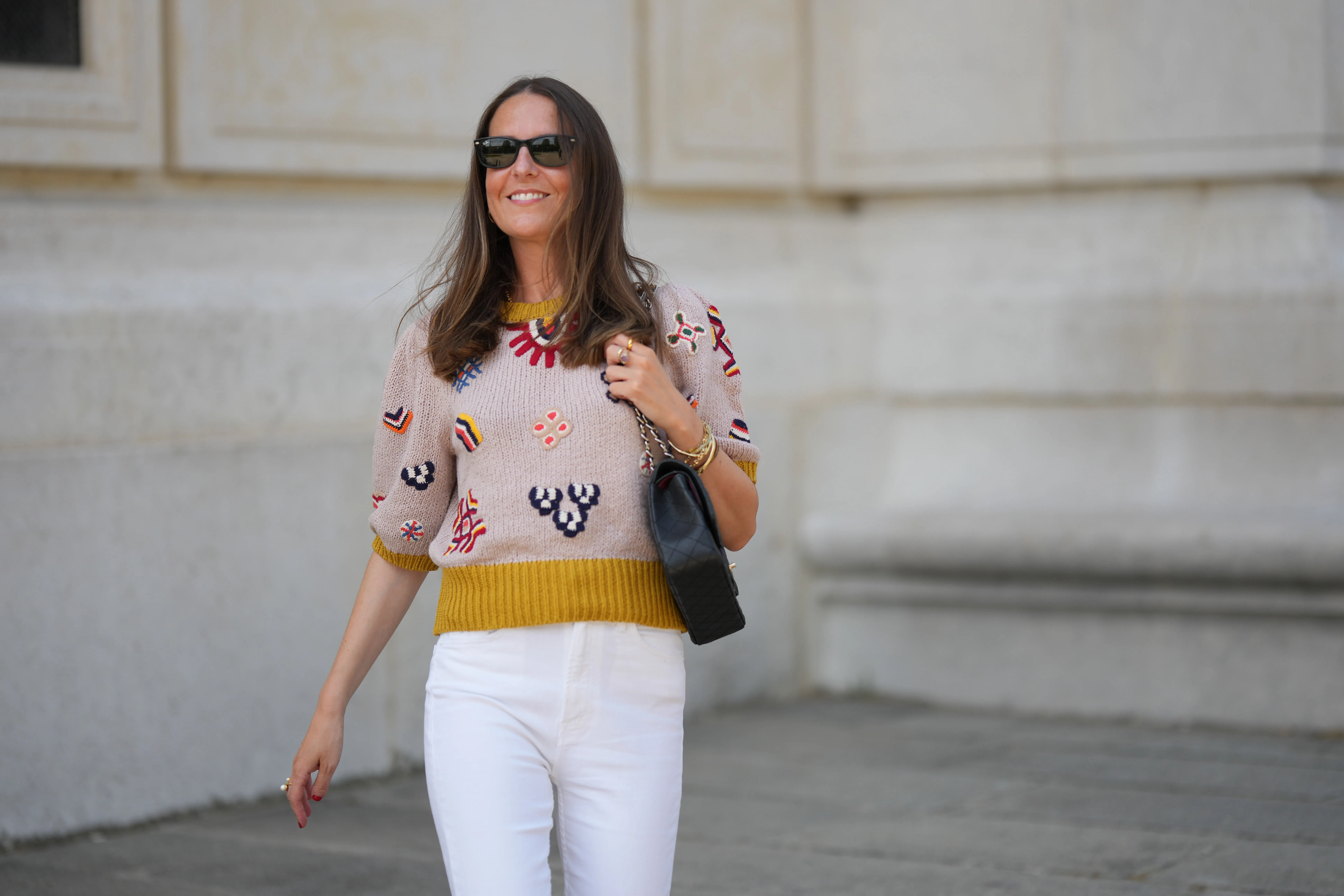 Alba Garavito Torre wears black sunglasses from Ray Ban, gold earrings, a gray with red / yellow / navy blue braided flower embroidered pattern / puffy short sleeves t-shirt, white high waist denim jeans pants from Mother Denim, black shiny leather Timeless shoulder bag from Chanel, during a street style fashion photo session, on June 06, 2023 in Paris, France.