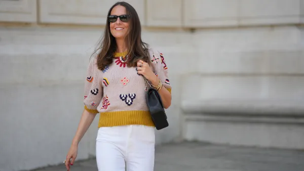 Alba Garavito Torre wears black sunglasses from Ray Ban, gold earrings, a gray with red / yellow / navy blue braided flower embroidered pattern / puffy short sleeves t-shirt, white high waist denim jeans pants from Mother Denim, black shiny leather Timeless shoulder bag from Chanel, during a street style fashion photo session, on June 06, 2023 in Paris, France.