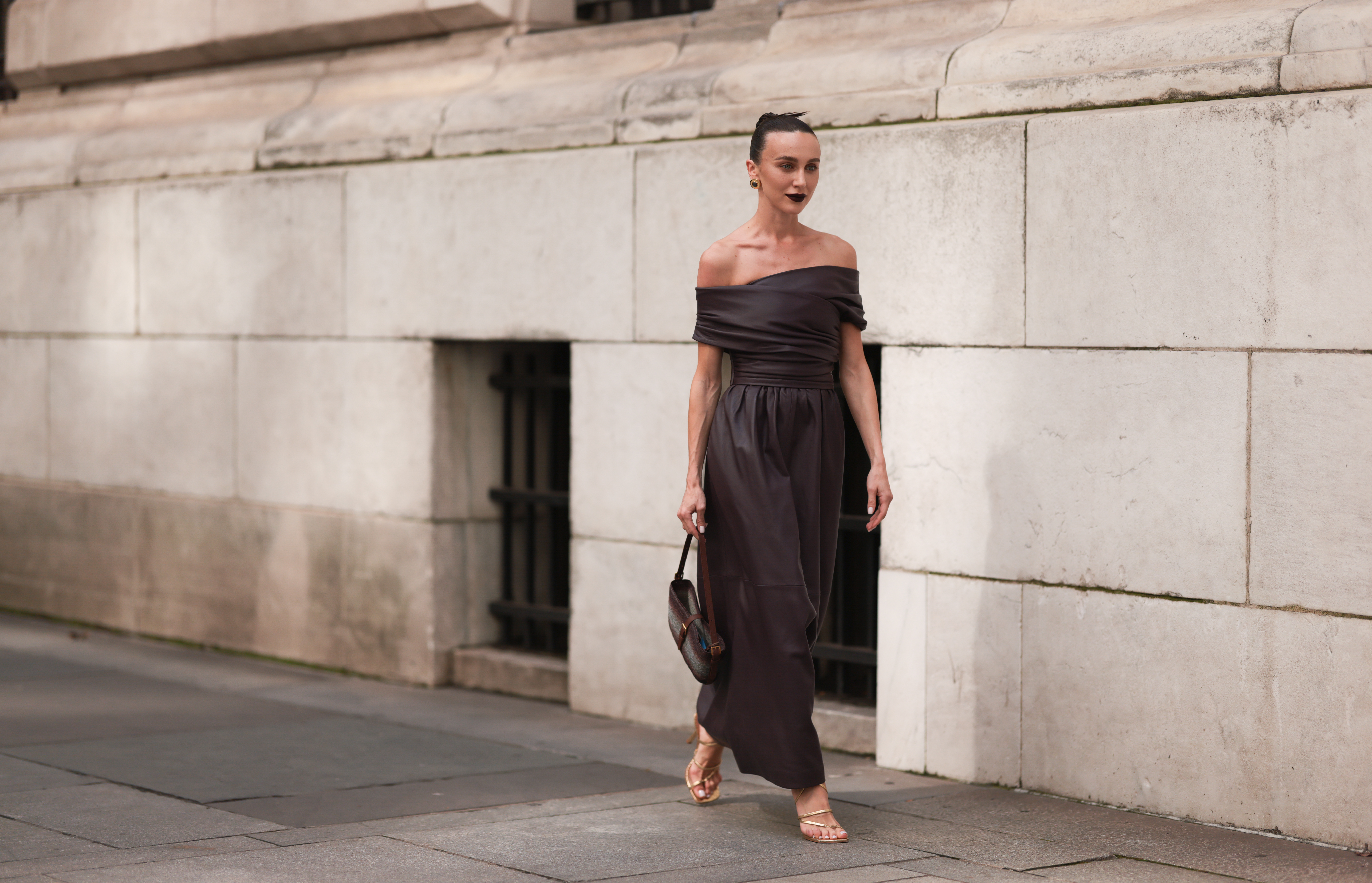 Mary Leest is seen outside Altuzarra show wearing golden earrings, brown leather wrapped around long dress, a brown handbag and golden lace up heels on September 11, 2023 in New York City.