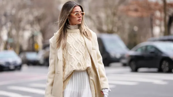 A guest wears yellow sunglasses, cream turtleneck long sleeve shirt, white pattern oversized buttoned up long sleeve shirt, cream knit oversized sweater, cream oversized wool coat, white mini skirt, outside Altuzarra, during the New York Fashion week Fall/Winter 2025 on February 8, 2025 in New York, New York.