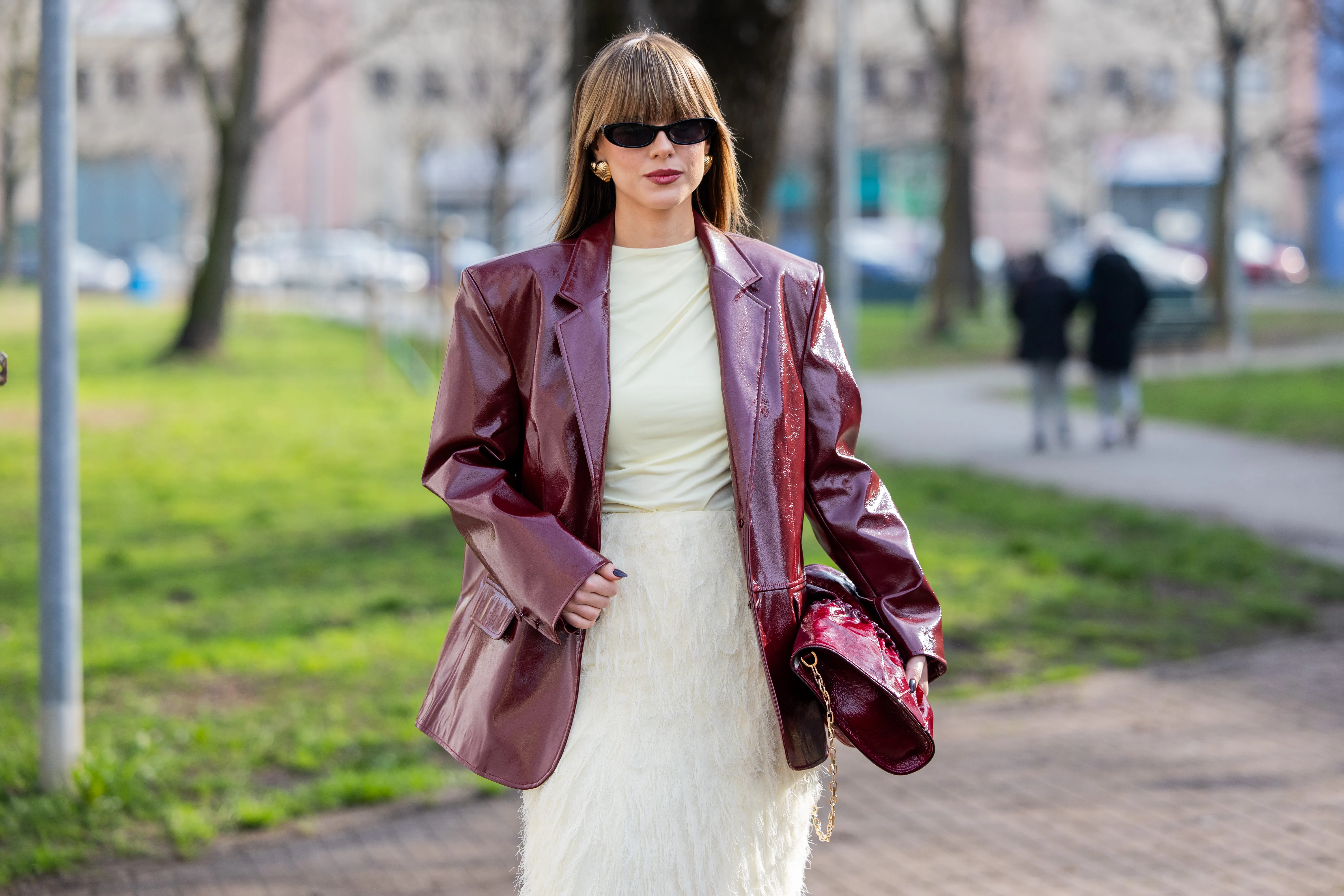 A guest wears burgundy vinyl jacket, beige skirt, pants, shirt, bag outside Jil Sander during the Milan Fashion Week Womenswear Fall/Winter 2025/2026 on February 26, 2025 in Milan, Italy.
