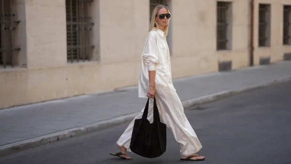 Mirja Klein is seen wearing a matching set consisting of a white striped oversized dobby-weave shirt with collar and buttons down in the front from H&M and a white striped straight pull-on trousers with loose fit and straight legs from H&M; a black suede tote bag with slouchy design and open top from COS; black oversized aviator sunglasses from Tom Ford; a pair of khaki green suede flip flops from A.EMERY on June 18, 2025 in Munich, Germany.
