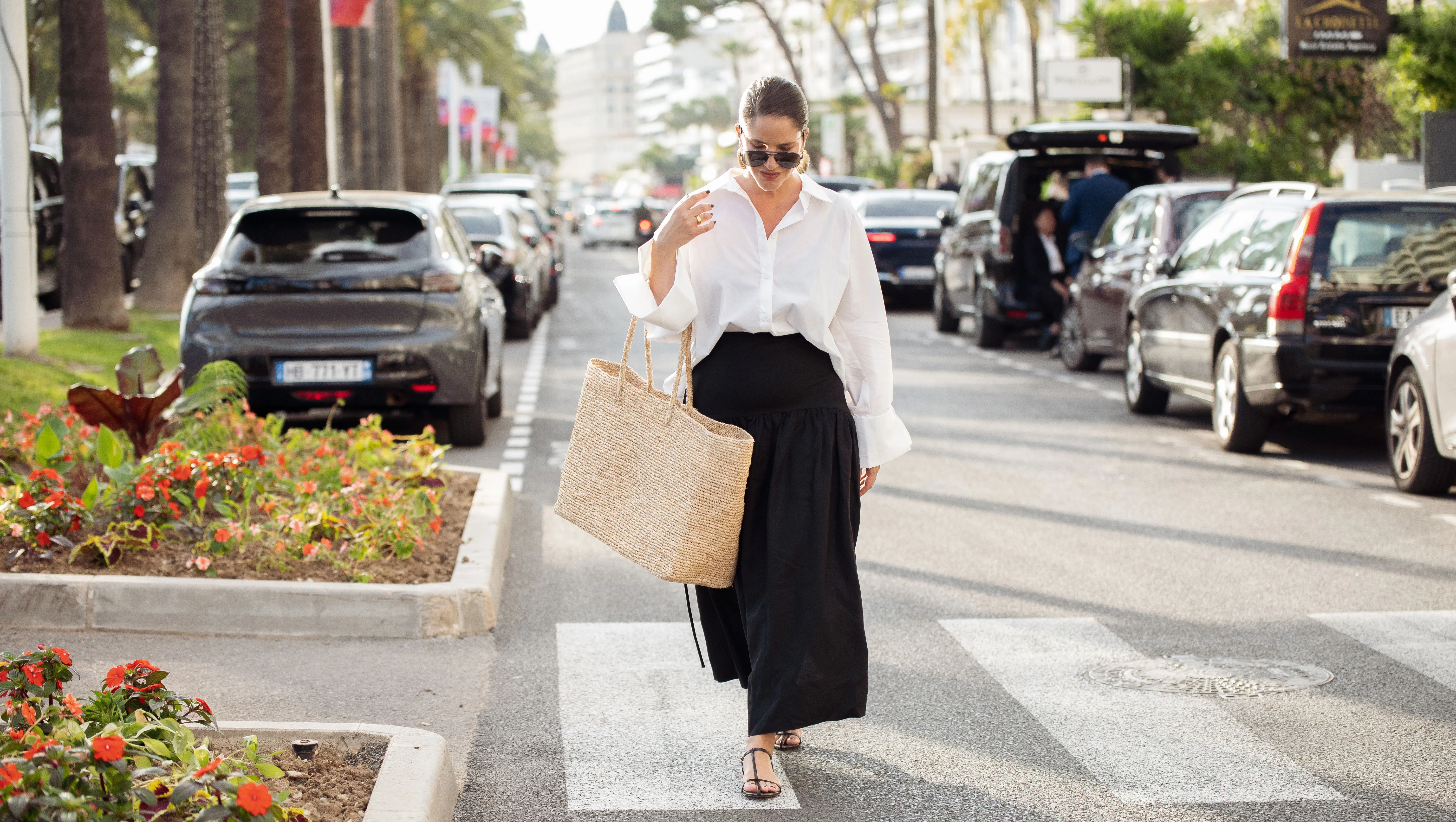 CANNES, FRANCE - MAY 15: Gili Biegun wears black long maxi skirt, white long sleeve shirt, oversized beige straw bag, sunglasses and sea shell golden earrings during day three of the 78th Cannes Film Festival on May 15, 2025 in Cannes, France. (Photo by Raimonda Kulikauskiene/Getty Images)