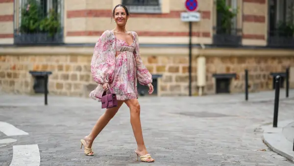 PARIS, FRANCE - AUGUST 04: Alba Garavito Torre wears earrings, a pale pastel pink mini low-neck gathered and pleated floral print dress with puff shoulders / sleeves and ruffles, a purple Jacquemus bag, Bottega Veneta wicker sandals shoes, on August 04, 2021 in Paris, France. (Photo by Edward Berthelot/Getty Images)