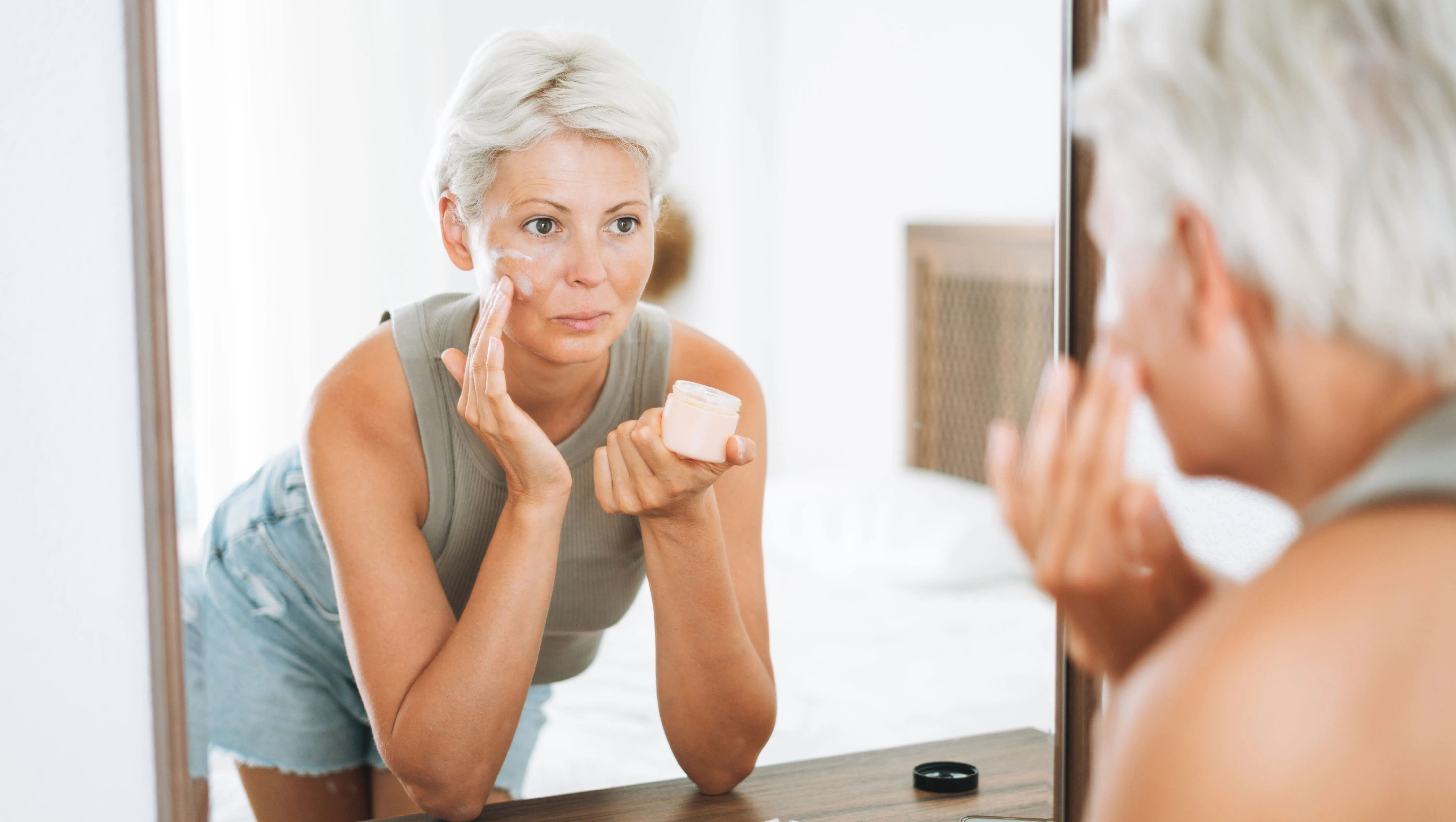 Beautiful woman with short hair applies cream to her face at home, morning skincare routine - stock photo