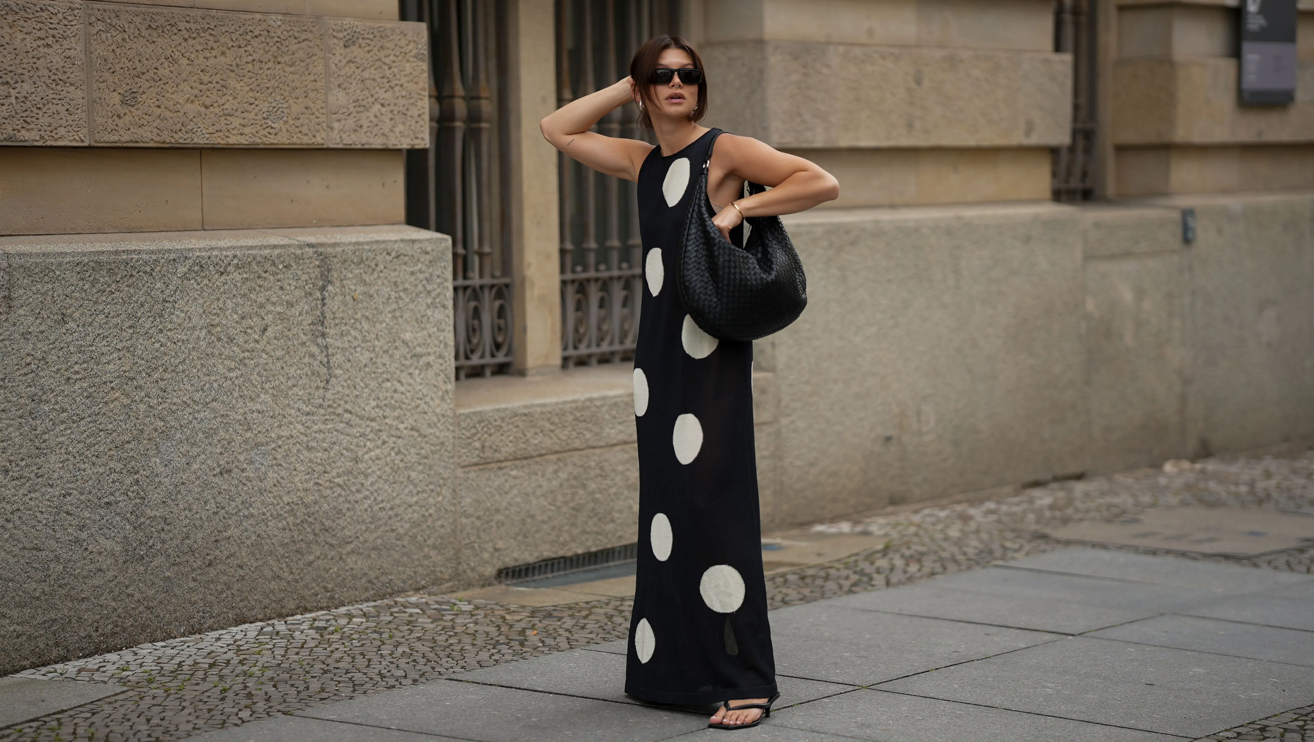 BERLIN, GERMANY - JUNE 24: Sophia Geiss is seen wearing a black and white long sleeveless polka dot knit dress with round neckline from Zara; a black Nana leather hobo bag with braided structure from abro; black PR 25YS sunglasses with rectangular biker shape from Prada; a pair of black thong sandals with kitten heel from LeGer by Lena Gercke; a pair of silver Harmonie big hoop earrings from black palms the label; a thin gold bangle from Daniel Wellington on June 24, 2025 in Berlin, Germany. (Photo by Moritz Scholz/Getty Images)