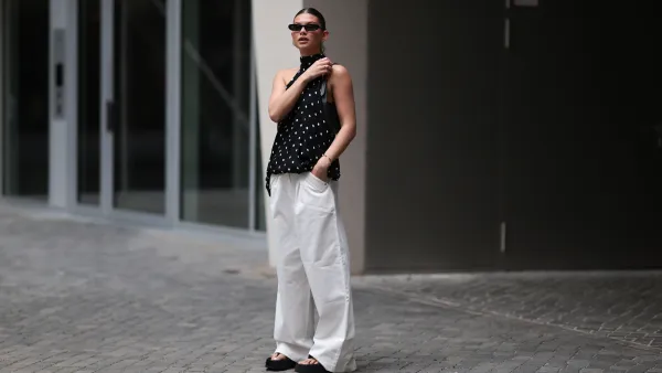 BERLIN, GERMANY - JUNE 04: Sophia Geiss is seen wearing silver hoop earrings in two different sizes; narrow oval black sunglasses from Saint Laurent; a silver nose ring; a flowy, backless halter-neck top in black with white polka dots from Zara; white wide-leg pants with a stretchy waistband and pocket details from The Room; a small rectangular black leather handbag with a gold YSL buckle from Yves Saint Laurent; a gold bangle; a silver minimalist ring; and black platform flip-flops from Zara on June 04, 2025 in Berlin, Germany. (Photo by Jeremy Moeller/Getty Images)