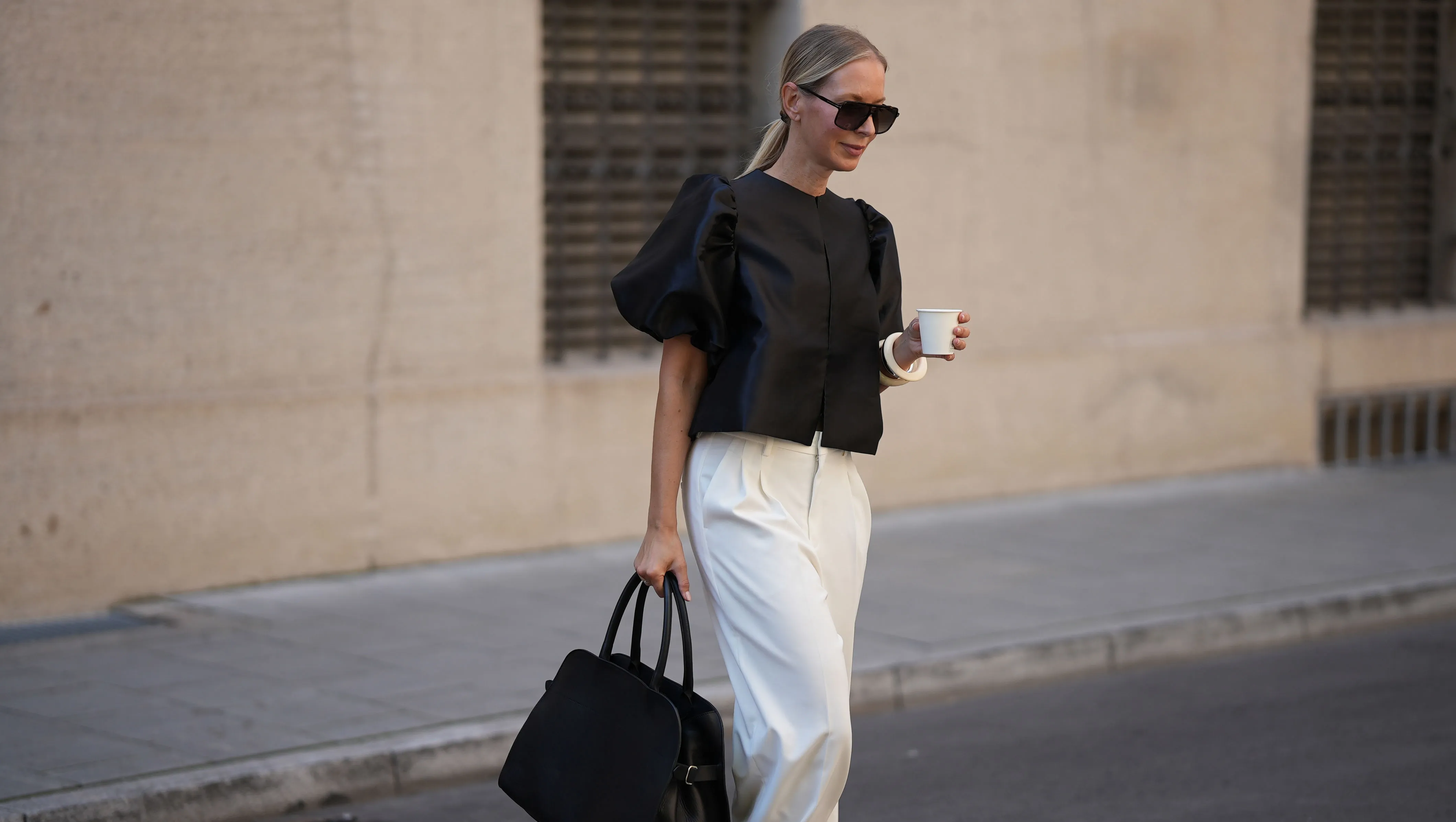 MUNICH, GERMANY - AUGUST 8: Mirja Klein is seen wearing a black short-sleeved Cleo blouse with voluminous puff shoulders and made of glossy material from By Malina; wide-leg off-white trousers with front pleats and elegant design from Rossi; a large structured black leather handbag with double top handles and adjustable straps on the sides from Liviana Conti; oversized aviator sunglasses in brown tortoiseshell acetate with brown shaded lenses from Tom Ford; an ecru colored Luca arm bangle set of two, made of synthetic resin from S&eacute;zane; her blonde hair is styled in a sleek low ponytail on August 8, 2025 in Munich, Germany. (Photo by Moritz Scholz/Getty Images)