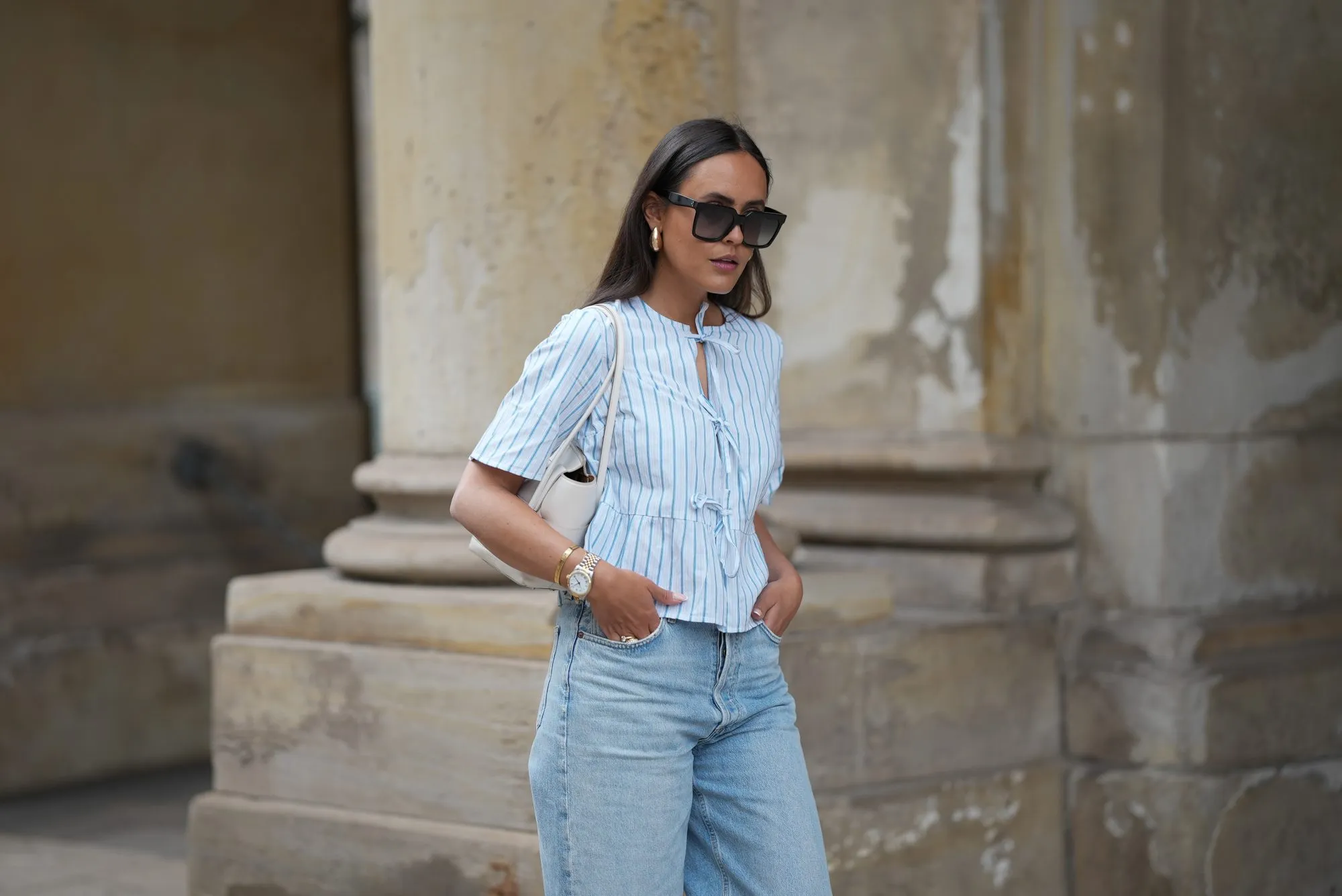 HAMBURG, GERMANY - MAY 7: Laura Noltemeyer is seen wearing a light indigo blue wide leg jeans from Agolde, a cotton puff sleeve blouse with ties in the front in white with blue stripes from S&eacute;zane, black oversized cat-eye acetate sunglasses from Celine, Arco handbag in white intrecciato leather from Bottega Veneta, big golden drop-shaped earrings, a small Lady-Datejust watch in gold-silver from Rolex, a golden LOVE bracelet from Cartier, stacked golden rings from Cartier on May 7, 2025 in Hamburg, Germany. (Photo by Moritz Scholz/Getty Images)