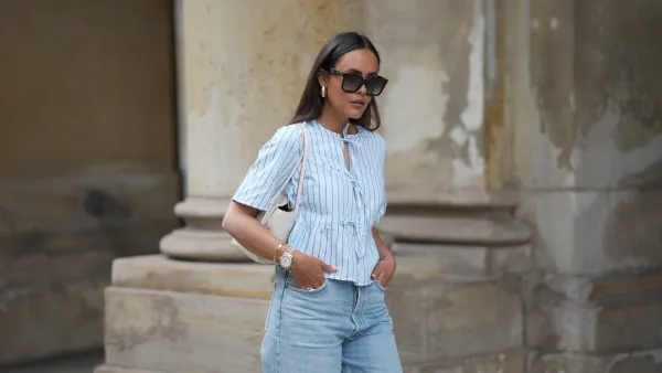 HAMBURG, GERMANY - MAY 7: Laura Noltemeyer is seen wearing a light indigo blue wide leg jeans from Agolde, a cotton puff sleeve blouse with ties in the front in white with blue stripes from Sézane, black oversized cat-eye acetate sunglasses from Celine, Arco handbag in white intrecciato leather from Bottega Veneta, big golden drop-shaped earrings, a small Lady-Datejust watch in gold-silver from Rolex, a golden LOVE bracelet from Cartier, stacked golden rings from Cartier on May 7, 2025 in Hamburg, Germany. (Photo by Moritz Scholz/Getty Images)
