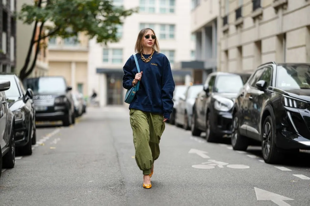 PARIS, FRANCE - NOVEMBER 09: Emy Venturini wears black Rayban sunglasses, a dark blue Supreme sweater, a gold Margiela necklace, a light blue leather Liase bag, khaki wide-leg pants, orange leather Roger Vivier high heels, during a street style fashion photo session, on November 09, 2024 in Paris, France. (Photo by Edward Berthelot/Getty Images)