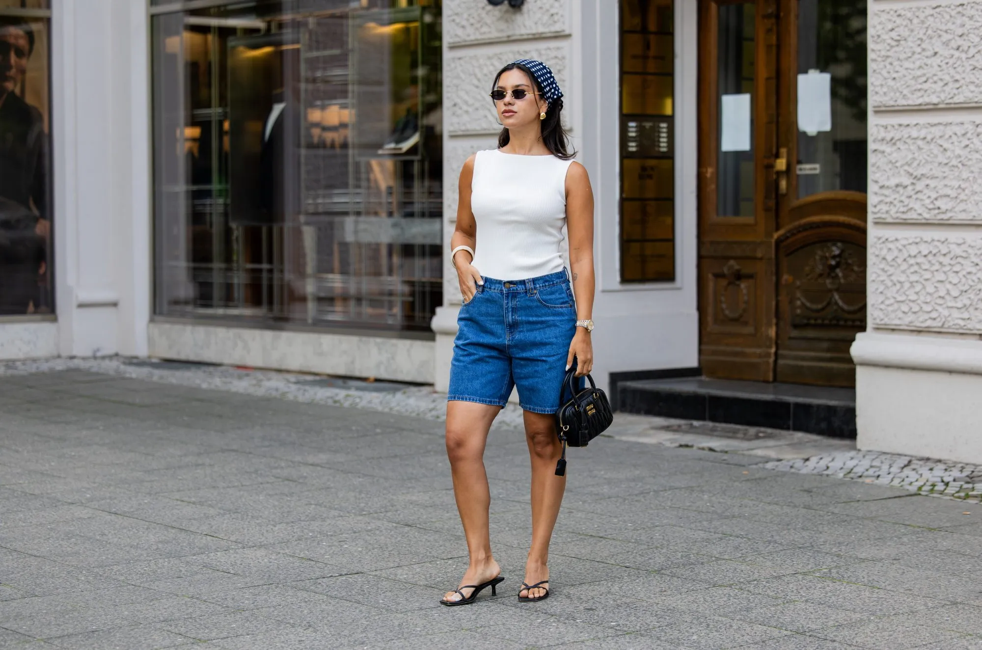 BERLIN, GERMANY - AUGUST 03: Bella Emar wears blue Polo Club Jeans Shorts & white Top, H&M sandals, Miu Miu Sunglasses & black Miu Miu bag, blue head scarf on August 03, 2025 in Berlin, Germany. (Photo by Christian Vierig/Getty Images)