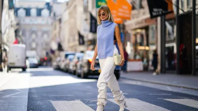 LONDON, ENGLAND - SEPTEMBER 15: Xenia Adonts wears sunglasses, a blue wool sleeveless turtleneck pullover, white pants, a bag featuring several attached squares, white boots, during London Fashion Week September 2019 on September 15, 2019 in London, England. (Photo by Edward Berthelot/Getty Images)