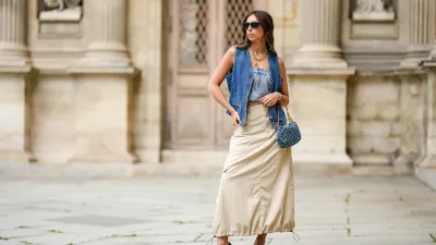 PARIS, FRANCE - APRIL 27: Gabriella Berdugo wears black sunglasses from Prada, a gold large necklace, silver and gold chain pendant necklaces, a navy blue denim sleeveless gilet from Mango, a pale blue denim shoulder-off buttoned top, a beige puffy long cargo maxi skirt from Filippa K , a blue denim ripped LV monogram pattern handbag from Louis Vuitton, dark green shiny leather pointed / gold metallic asymmetric heels shoes from Charles Jourdan, during a street style fashion photo session, on April 27, 2023 in Paris, France. (Photo by Edward Berthelot/Getty Images)