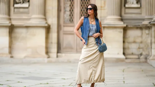 PARIS, FRANCE - APRIL 27: Gabriella Berdugo wears black sunglasses from Prada, a gold large necklace, silver and gold chain pendant necklaces, a navy blue denim sleeveless gilet from Mango, a pale blue denim shoulder-off buttoned top, a beige puffy long cargo maxi skirt from Filippa K , a blue denim ripped LV monogram pattern handbag from Louis Vuitton, dark green shiny leather pointed / gold metallic asymmetric heels shoes from Charles Jourdan, during a street style fashion photo session, on April 27, 2023 in Paris, France. (Photo by Edward Berthelot/Getty Images)