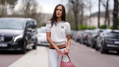 PARIS, FRANCE - MARCH 09: Amalie Bladt wears short sleeve Lacoste sweater, white pleated Lacoste midi skirt, a gold bracelet, a gold watch, shiny dark red Lacoste leather bag, outside Lacoste, during the Paris Fashion week Women's Fall/Winter 2025-2026 on March 9, 2025 in Paris, France. (Photo by Edward Berthelot/Getty Images)