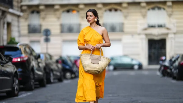 PARIS, FRANCE - AUGUST 12: Ketevan Giorgadze @katie.one wears a one shoulder cut out maxi dress in orange from Mango, oversized golden hoop earrings from Zara, flip flop heeled black sandals shoes from APC Paris, a Le Grand Panier beach straw bag by Jacquemus, on August 12, 2021 in Paris, France. (Photo by Edward Berthelot/Getty Images)