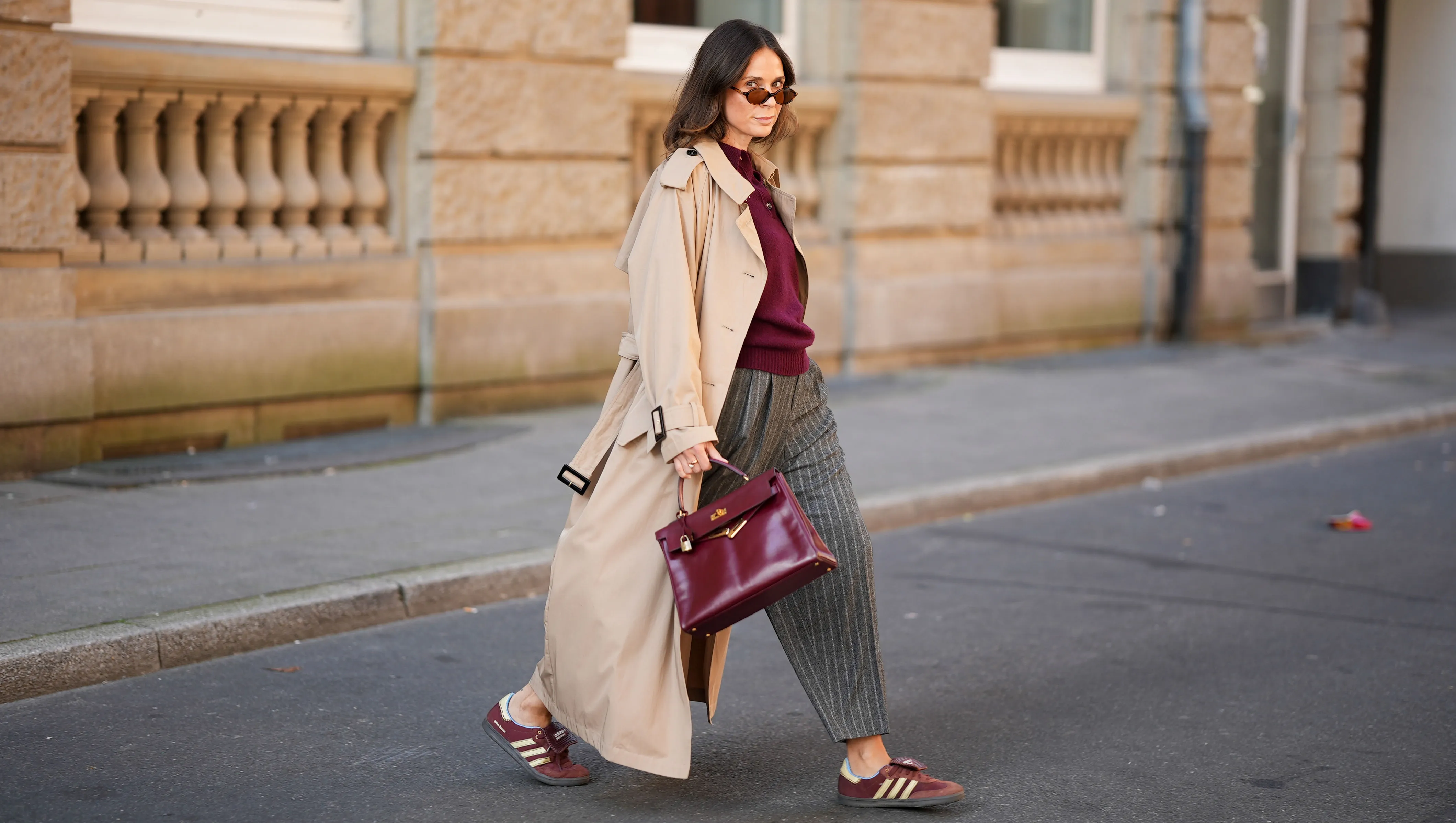 DUESSELDORF, GERMANY - AUGUST 19: Patricia Wirschke is seen wearing a Anna V Berg burgundy knit polo sweater with three buttons, collar and ribbed hem; a classic beige long Herno trench coat, with a notched collar, storm flap, and belted cuffs; a pair of high-waisted, wide-leg, ankle length Rossi pants that feature a gray pinstripe pattern with tailored pleats and loose silhouette; a pair of burgundy suede Adidas Samba X Wales Bonner sneakers with cream stripes; a structured, glossy burgundy leather Hermes Kelly bag with gold-tone hardware; a pair of Miu Miiu oval-shaped tortoiseshell sunglasses; her brown hair is styled in a straight, shoulder-length look with a middle part on August 19, 2025 in Duesseldorf, Germany. (Photo by Moritz Scholz/Getty Images)