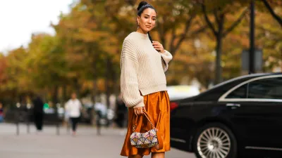 PARIS, FRANCE - SEPTEMBER 28: Tamara Kalinic wears a wool pullover, an orange shiny silky skirt, earrings, a Fendi bag, black high heeled boots, outside CDG Comme des Garçons, during Paris Fashion Week - Womenswear Spring Summer 2020 on September 28, 2019 in Paris, France. (Photo by Edward Berthelot/Getty Images)