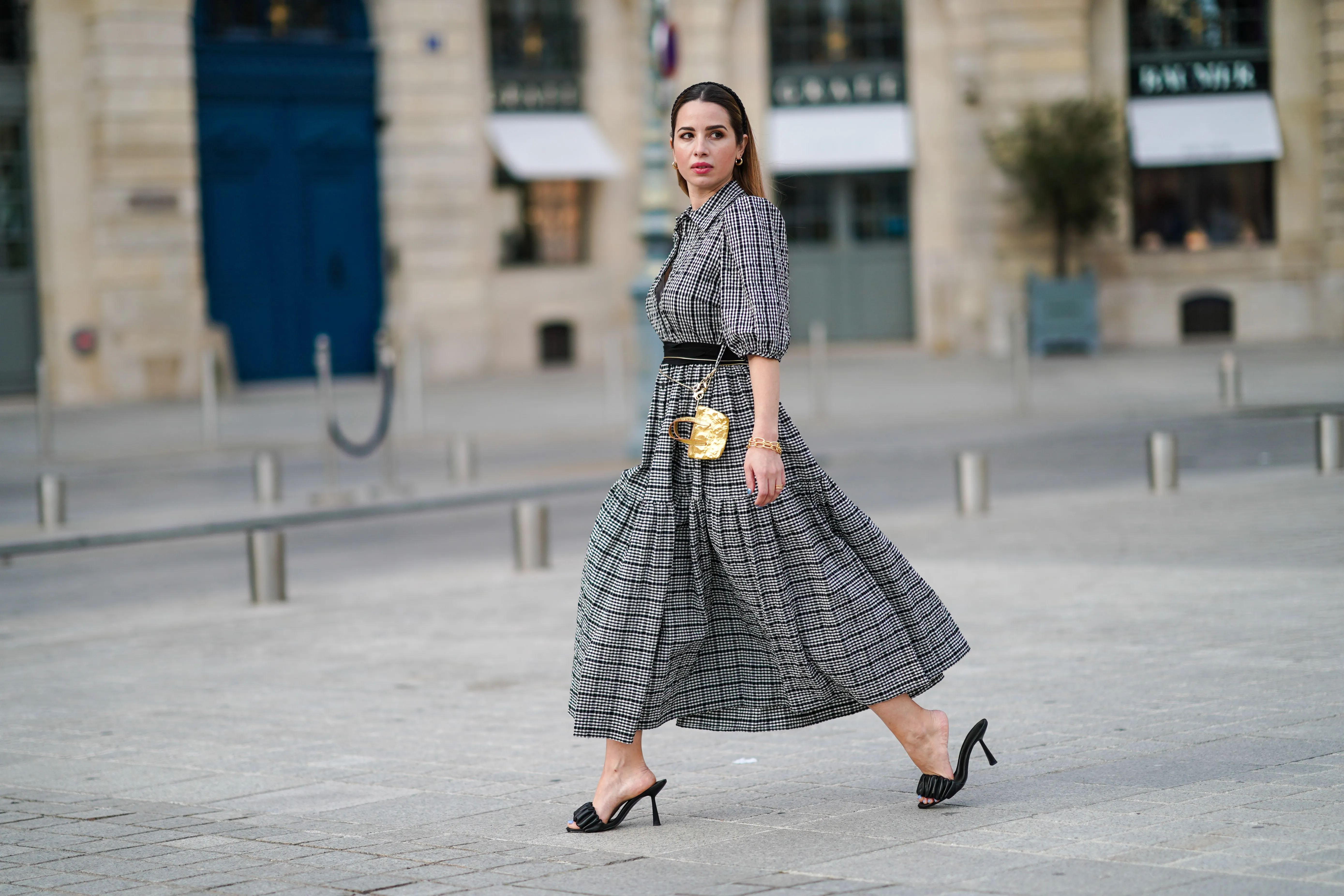Maria Rosaria Rizzo @lacoquetteitalienne wears earrings, a grey gathered checked dress with puff sleeves from Parosh, a golden bracelet, a golden mini bag from Duren Japan, black leather sandals shoes from LPA, golden jewelry from & Other Stories, on March 03, 2021 in Paris, France.