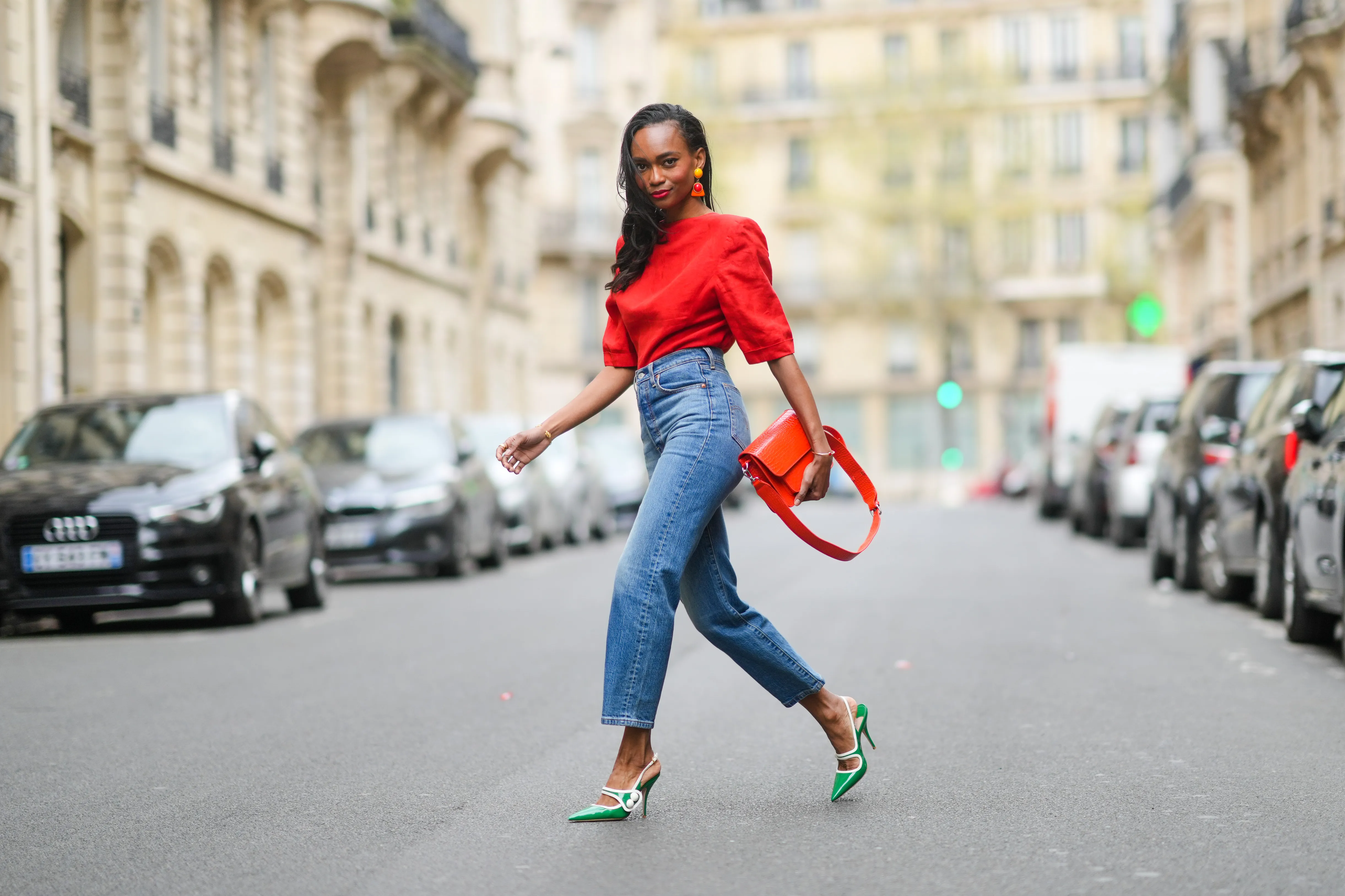 PARIS, FRANCE - APRIL 18: Emilie Joseph @in_fashionwetrust wears a red vintage linen power shoulder top worn backwards with plunging neckline in the back, blue denim high rise straight ribcage jeans from Levi's, green two-toned patent leather pointy sling back sandals / pumps from Miumiu, a red vegan embossed leather bag from Hvisk, clip-on Vintage colorblock ceramic earrings, on April 18, 2021 in Paris, France. (Photo by Edward Berthelot/Getty Images)