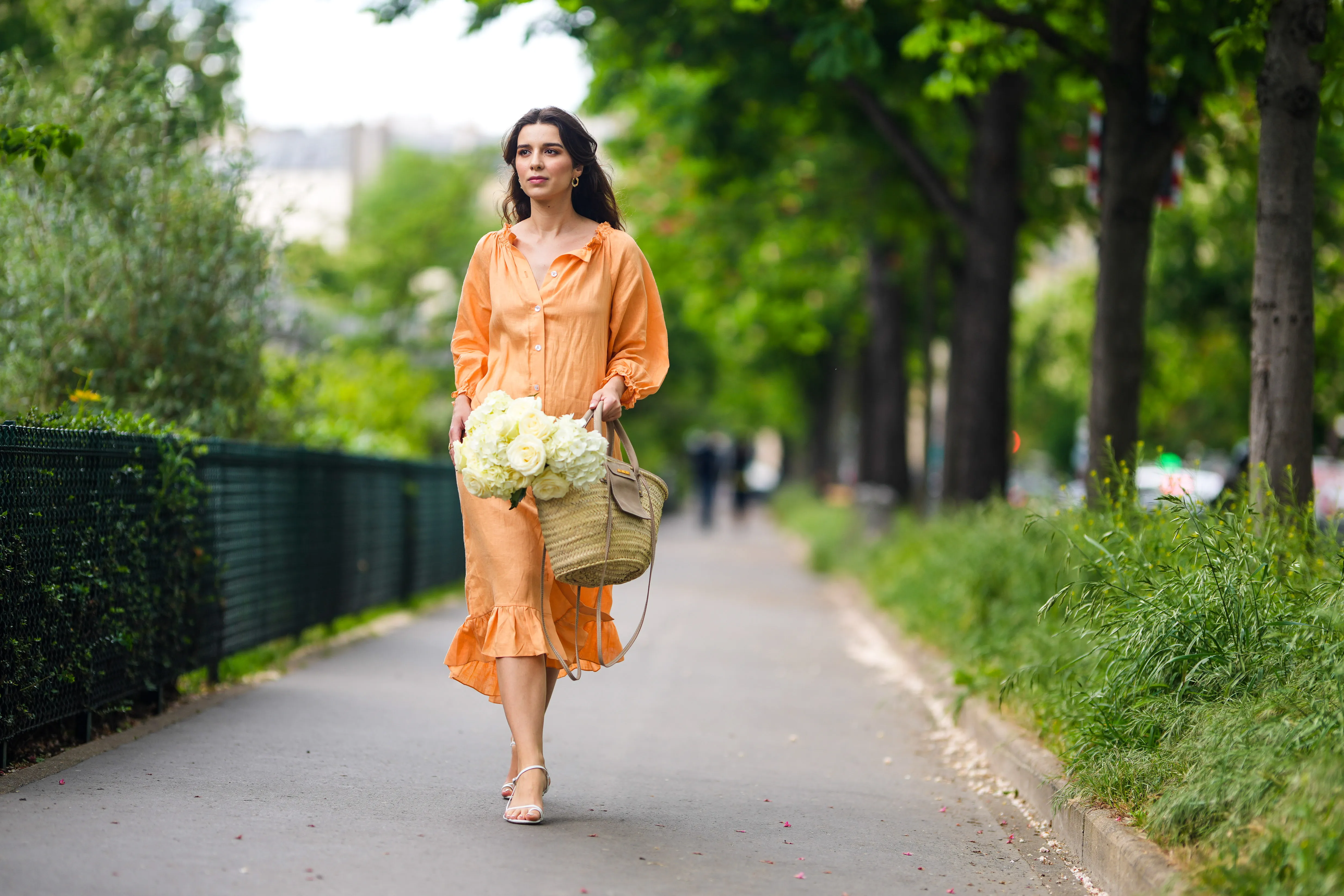 PARIS, FRANCE - MAY 10: Ketevan Giorgadze @katie.one wears gold earrings, a long buttoned coral loungewear linen The Sleeper dress with puffy sleeves, gold rings, a wicker with brown shiny leather detail Le Panier Soleil Jacquemus tote-bag, white strappy low heeled Raye sandals, on May 10, 2021 in Paris, France. (Photo by Edward Berthelot/Getty Images)