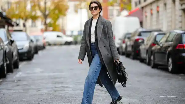 Katie Giorgadze @katie.one wears black sunglasses, a white latte ribbed high neck wool pullover, a black long blazer jacket, a black and white print pattern long oversized wool coat, high waist blue denim large ripped pants, a black shiny leather crocodile print pattern shoulder bag from Balenciaga, black shiny leather block heels loafers from Prada, on November 26, 2021 in Paris, France.