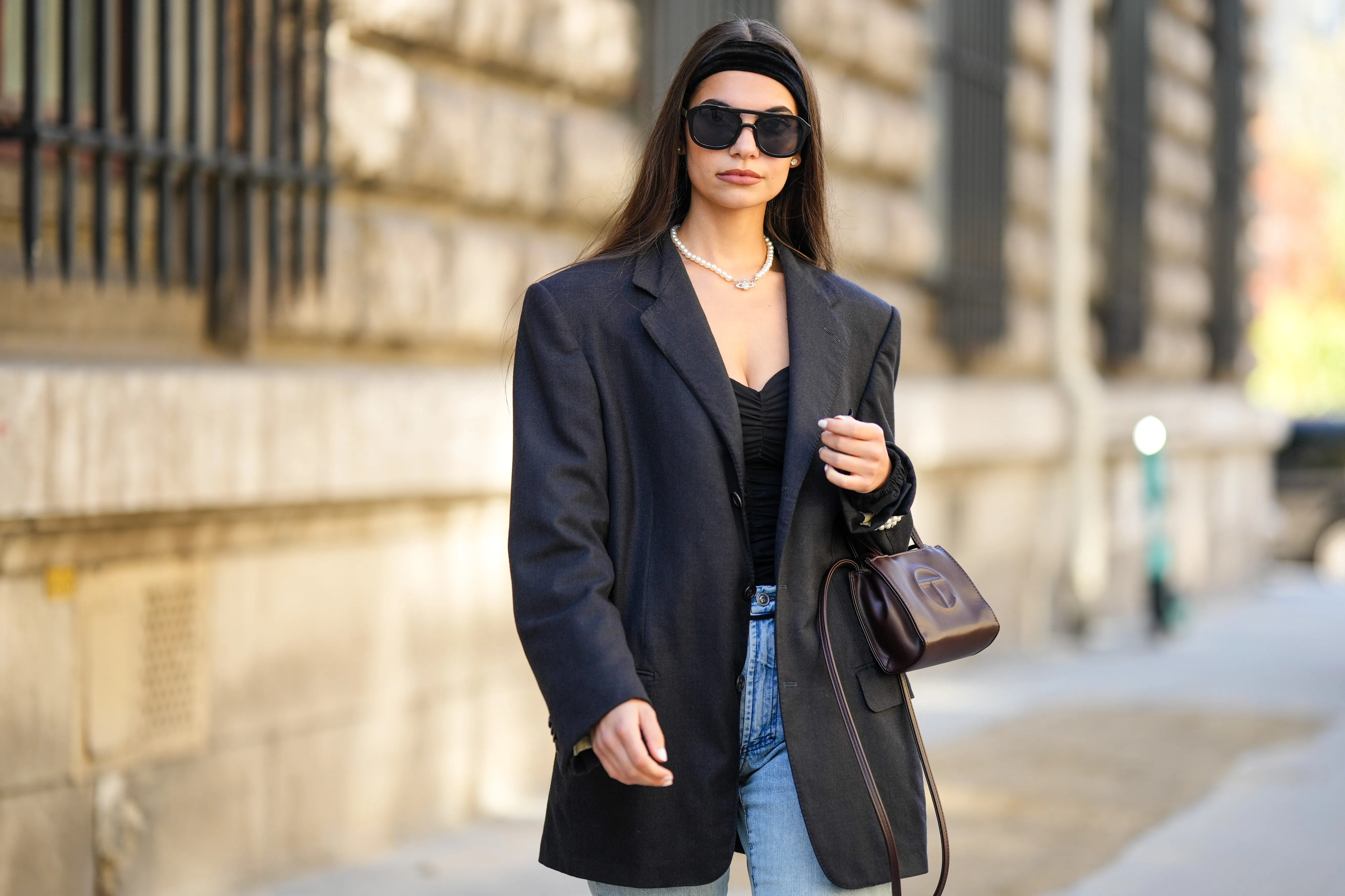 PARIS, FRANCE - SEPTEMBER 30: Bengi Guzel wears a black large velvet headband, silver earrings, a white pearls with diamonds logo necklace from Vivienne Westwood, a black shoulder-off body, a black blazer jacket, blue denim large pants, a brown shiny leather handbag from Telfar, outside Loewe, during Paris Fashion Week - Womenswear Spring/Summer 2023, on September 30, 2022 in Paris, France. (Photo by Edward Berthelot/Getty Images)