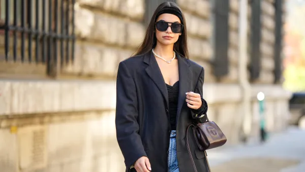 PARIS, FRANCE - SEPTEMBER 30: Bengi Guzel wears a black large velvet headband, silver earrings, a white pearls with diamonds logo necklace from Vivienne Westwood, a black shoulder-off body, a black blazer jacket, blue denim large pants, a brown shiny leather handbag from Telfar, outside Loewe, during Paris Fashion Week - Womenswear Spring/Summer 2023, on September 30, 2022 in Paris, France. (Photo by Edward Berthelot/Getty Images)