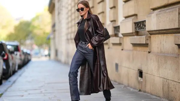 Diane Batoukina wears black sunglasses, a black t-shirt, a dark brown shiny leather long coat, a black shiny grained leather Kelly small belt from Hermes, black denim large pants, a black shiny leather Timeless handbag from Chanel, black shiny leather heels ankle boots , during a street style fashion photo session, on October 26, 2022 in Paris, France.
