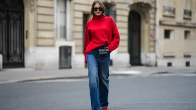 Diane Batoukina wears black sunglasses, a red wool ribbed turtleneck pullover, a black shiny leather belt bag from Chanel, blue faded denim wide legs pants, red shiny varnished leather pointed pumps heels shoes, during a street style fashion photo session, on November 10, 2022 in Paris, France.