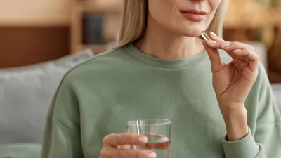 Minimal close up of adult woman taking vitamin pill and holding glass of water at home copy space