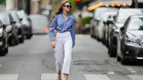 Segolene Hyppolite wears sunglasses, a blue and white oversized shirt from Tommy Hilfiger, a raffia beige bag from Vanessa Bruno, high waist white denim pants from Vanessa Bruno, Chanel slingback shoes in blue denim with black tips, during a street style fashion photo session, on May 20, 2024 in Paris, France.