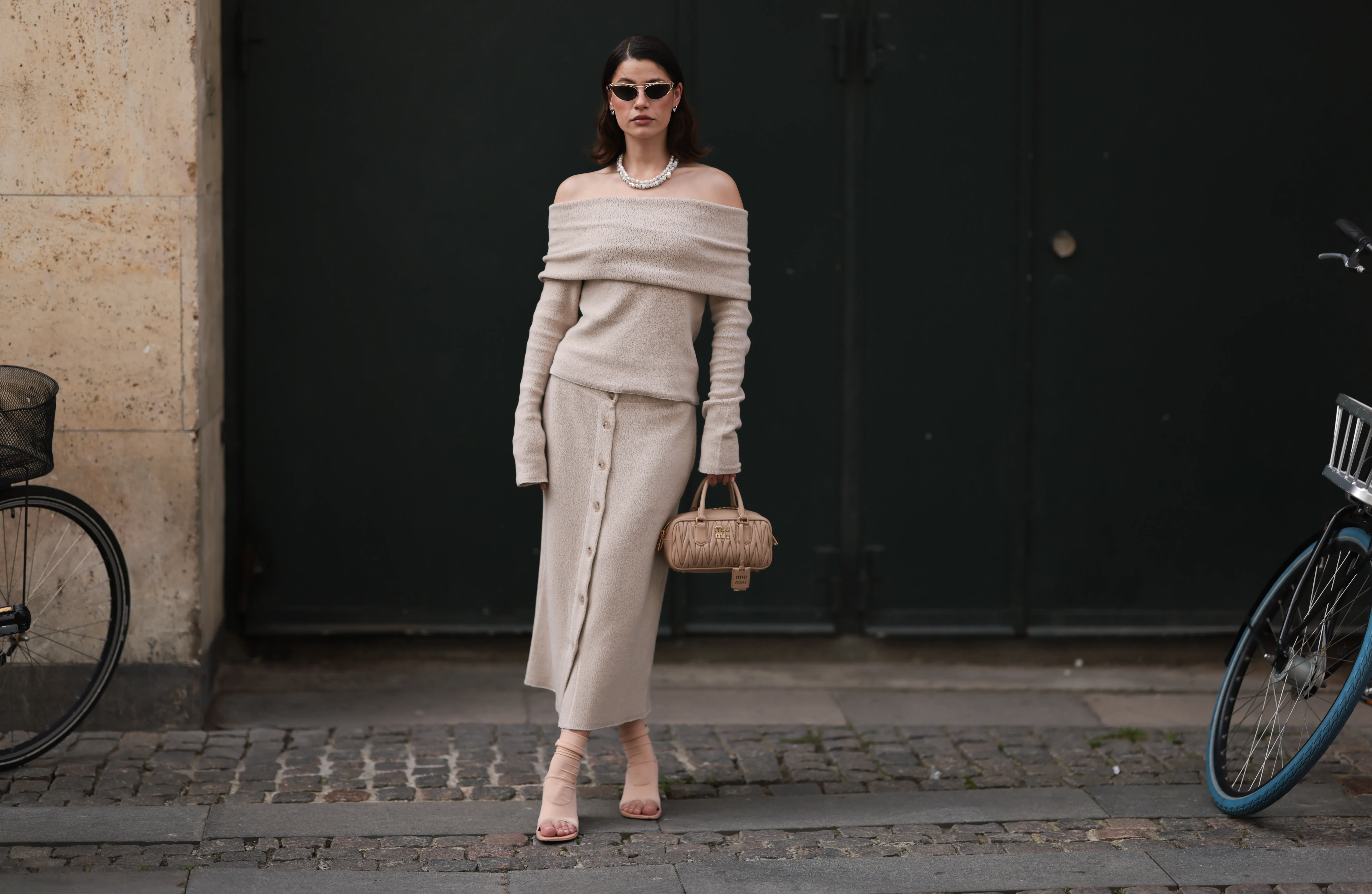 COPENHAGEN, DENMARK - AUGUST 06: Lea Naumann is seen wearing oval sunglasses with a golden frame, small silver hoop earrings with heart pendants, a pearl necklace, and a silver necklace with various pendants from Pandora, a beige fleece Bardot jumper with a matching buttoned midi skirt, a beige leather bag from Miu Miu, and beige ankle-high thong sandals before the Filippa K SS25 Lunch Event during day two of the Copenhagen Fashion Week (CPHFW) SS25 on August 06, 2024 in Copenhagen, Denmark. (Photo by Jeremy Moeller/Getty Images)