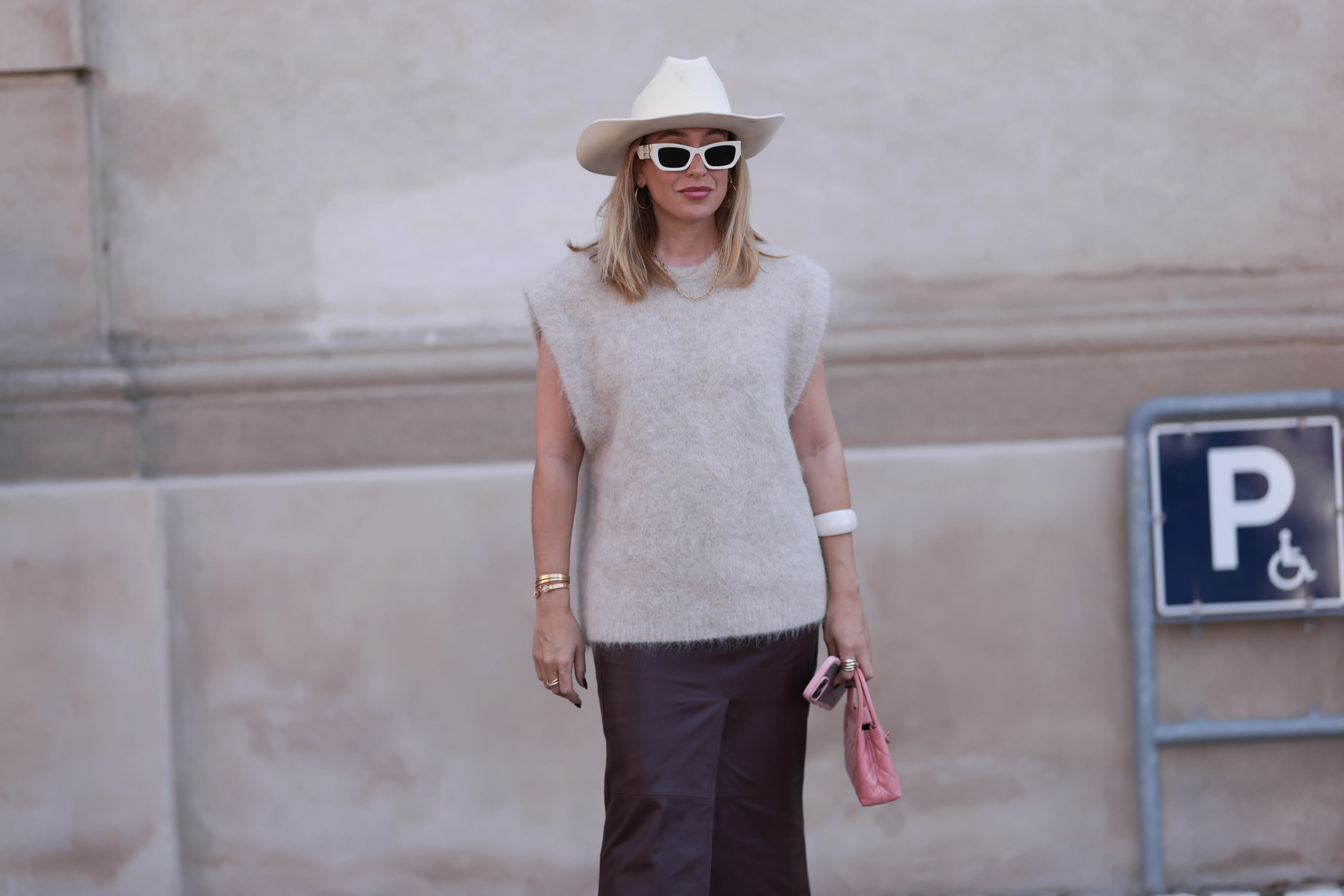 COPENHAGEN, DENMARK - AUGUST 07: Sonia Lyson is seen wearing a white cowboy hat, rectangular cat-eye sunglasses with bold white frame and wide temple from Miu Miu, golden hoop earrings, a golden chain necklace, a grey oversized wool tank top from The Garment, several golden bracelets, including the yellow-gold &ldquo;Love&ldquo; bracelet from Cartier, a bold white bangle, several rings in gold and silver, a small rectangular quilted pink leather bag from Chanel, and an ankle-length dark purple leather skirt from Dorothee Schumacher before The Garment Show during day three of the Copenhagen Fashion Week (CPHFW) SS25 on August 07, 2024 in Copenhagen, Denmark. (Photo by Jeremy Moeller/Getty Images)