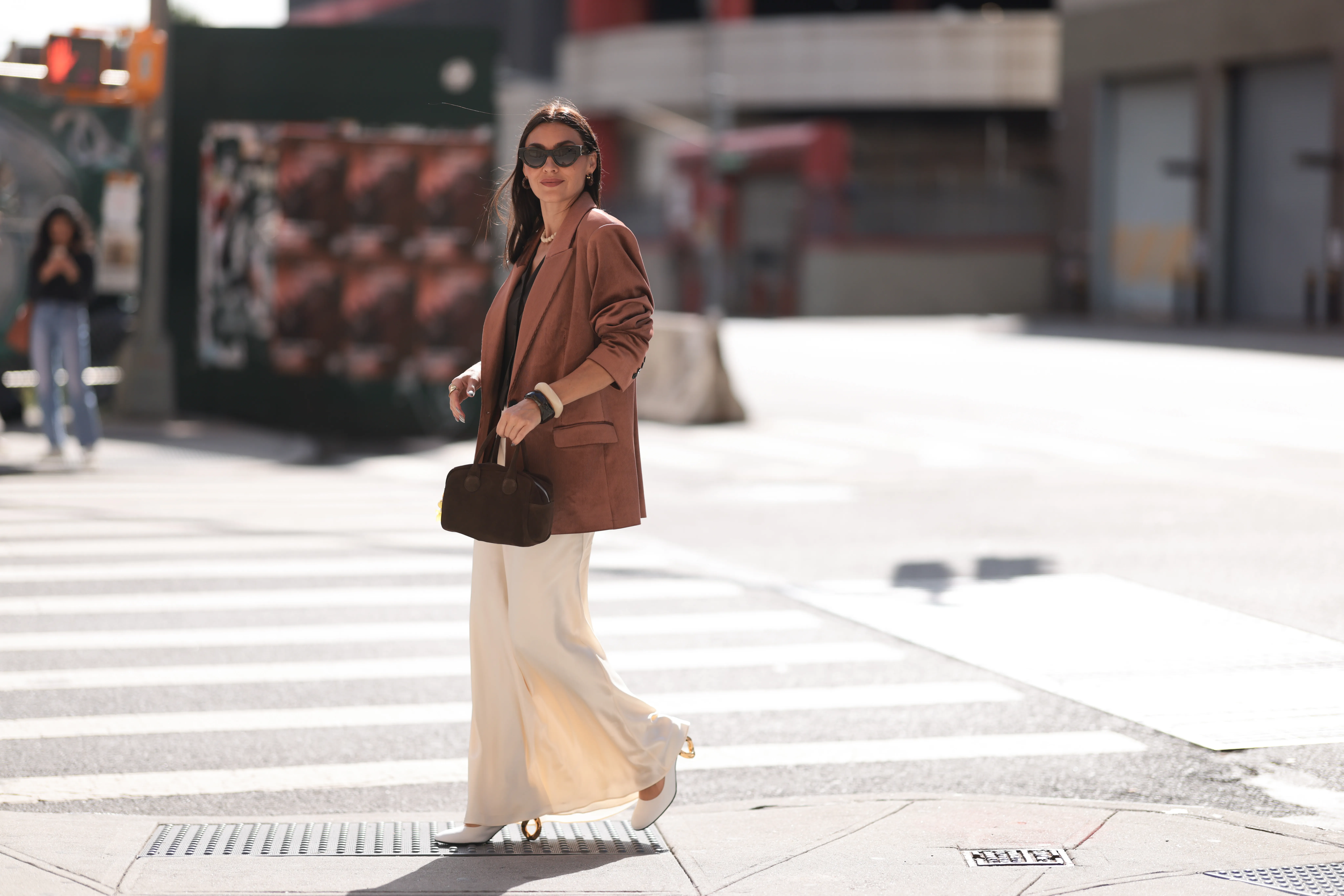Yana Echko seen wearing YSL brown sunglasses, Bottega Veneta brown leather earrings, white pearl necklace, The Frankie Shop brown pinstripe vest, Express light brown corduroy blazer jacket, Reformation cream white maxi silk long skirt, MARGE SHERWOOD brown suede leather small bag, Kenneth Jay Lane gold ring, cream white / brown bangle and JW Anderson white leather pumps, outside the Bach Mai show, during the New York Fashion Week, on September 08, 2024 in New York City.