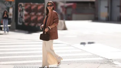 Yana Echko seen wearing YSL brown sunglasses, Bottega Veneta brown leather earrings, white pearl necklace, The Frankie Shop brown pinstripe vest, Express light brown corduroy blazer jacket, Reformation cream white maxi silk long skirt, MARGE SHERWOOD brown suede leather small bag, Kenneth Jay Lane gold ring, cream white / brown bangle and JW Anderson white leather pumps, outside the Bach Mai show, during the New York Fashion Week, on September 08, 2024 in New York City.