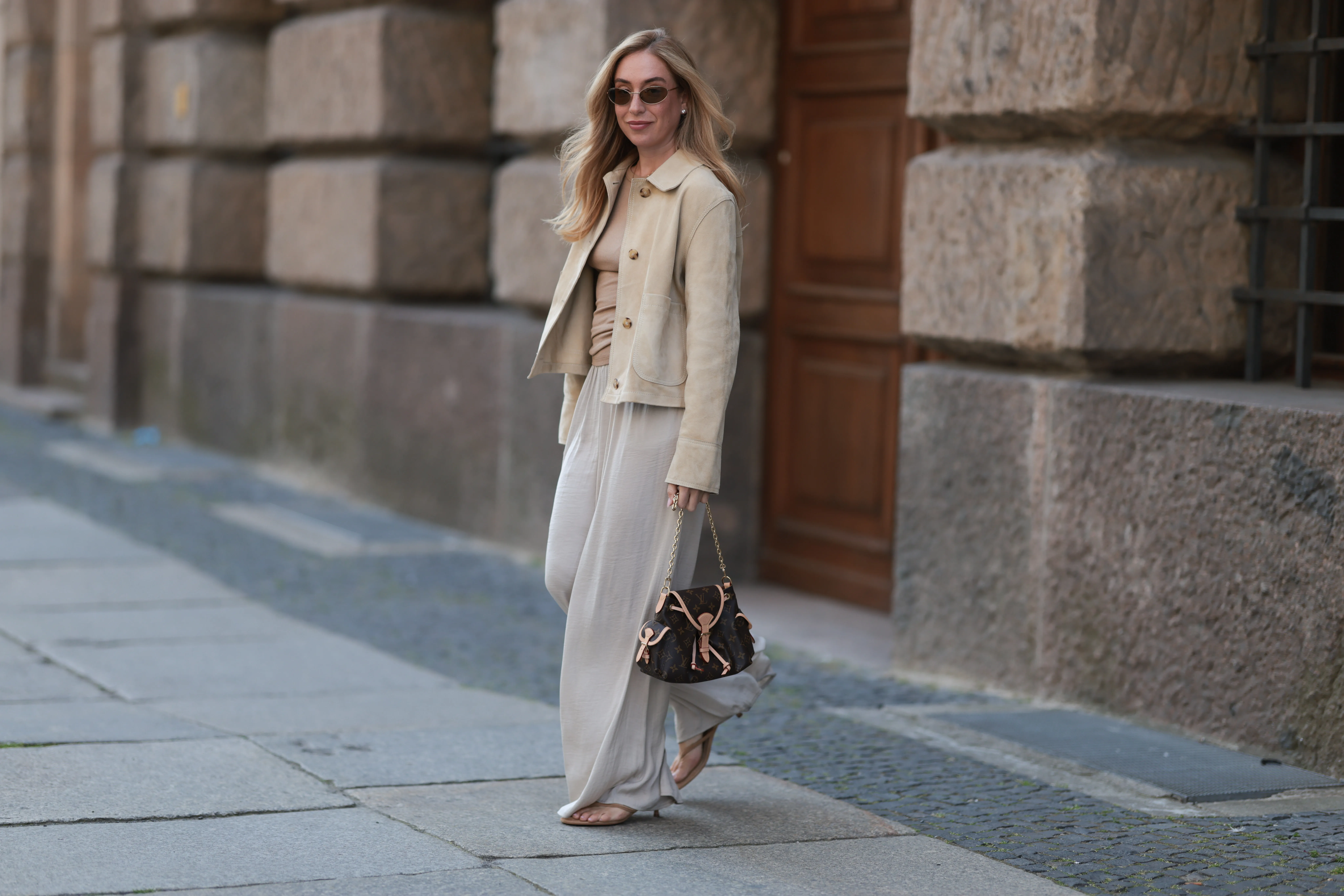 Sonia Lyson is seen wearing oval cat-eye sunglasses with brown lenses and a thin silver metal frame from Prada; several earrings and stud earrings; a fine gold necklace with a round pendant; a beige suede jacket with large collar and white decorative seams from Zara; a light brown ribbed top with high round neckline from Munthe underneath; a brown leather &ldquo;Odyssee&ldquo; handbag from Louis Vuitton; wide-leg cream-white pants from Zara; and beige suede heeled sandals, also from Zara on June 20, 2025 in Berlin, Germany.