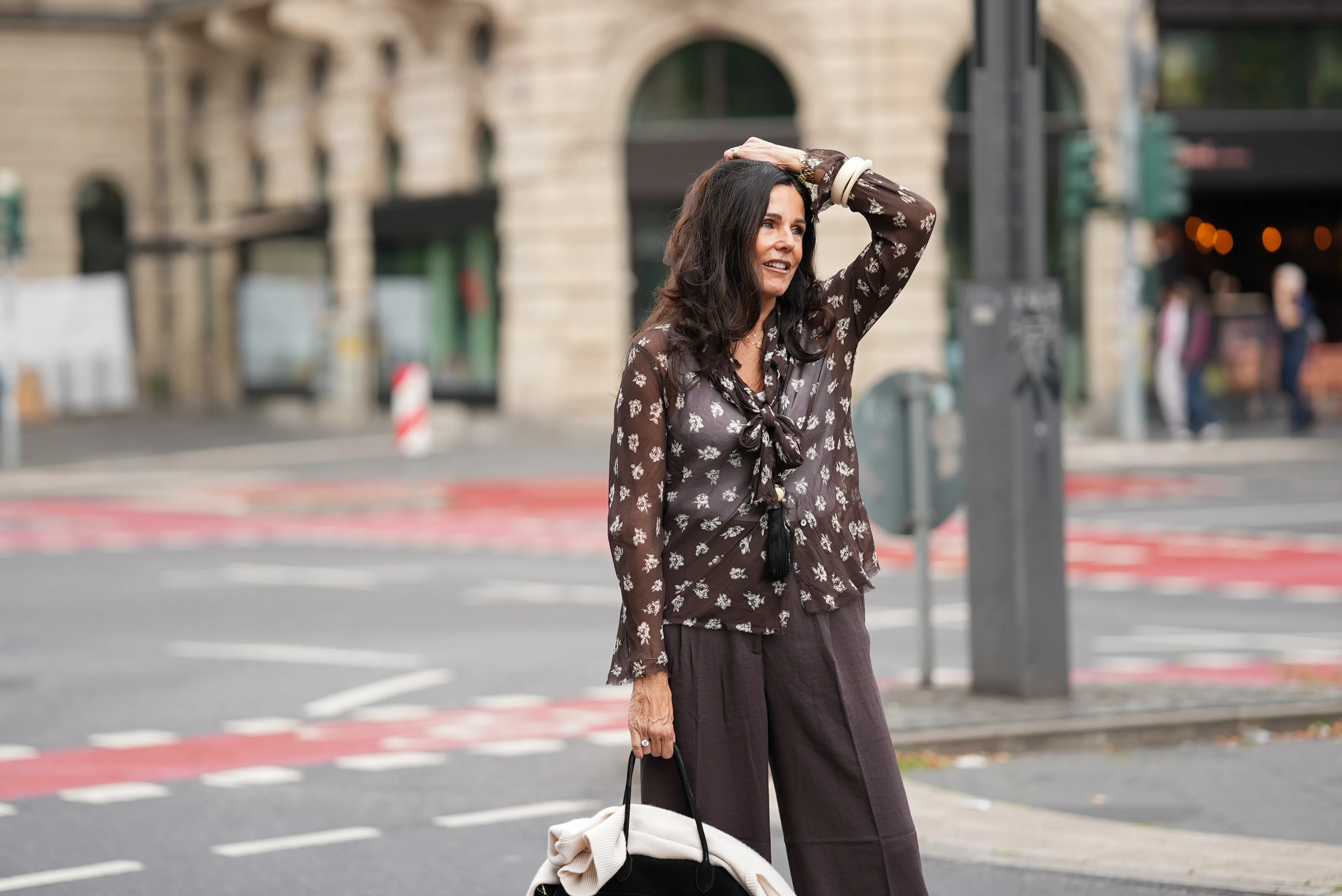 Angelika Hanel is seen wearing a chocolate brown flowing shirt with scarf collar, semi-sheer fabric, cream white floral print and button-up front from Massimo Dutti; a soft beige v-neck cashmere pullover with a relaxed silhouette and subtle ribbed cuffs and hem from Sa Su Phi; dark brown wide-leg linen blend trousers with a relaxed fit from H&M; a large black suede top-handle Soft Margaux 17 bag with softly structured sides, gold-tone buckles on the sides and a curved silhouette from The Row; a long black ceramic tassel cord necklace from Massimo Dutti; a golden necklace with a vintage Alhambra pendant in the shape of a cloverleaf from Van Cleef & Arpels; a golden Day-Date wristwatch from Rolex; a white gold pav&eacute; diamond tennis bracelet; an ecru colored Luca arm cuff set of two, made of synthetic resin from S&eacute;zane; a ring stacked with gold bands and a diamond from Marr&eacute;; a diamond ring on July 27, 2025 in Frankfurt am Main, Germany.