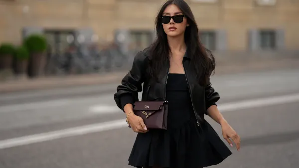 COPENHAGEN, DENMARK - AUGUST 5: Milena Karl, attending the Pandora Event during Copenhagen Fashion Week SS26, is seen wearing a black strapless Faille Halter Mini dress with a ruched waistline and flared skirt from Helsa; a black leather bomber jacket with structured shoulders, elastic cuffs and waistband and zip fastening from Khaite; sheer black tights; a burgundy leather Kelly Elan Sellier handbag with silver-tone hardware from Hermès; a gold charm bracelet adorned with crystal and enamel details from Pandora; narrow black rectangular Wayfarer sunglasses from Ray-Ban; her long dark hair is worn down in soft waves with a center part during Copenhagen Fashion Week day two on August 5, 2025 in Copenhagen, Denmark. (Photo by Moritz Scholz/Getty Images)