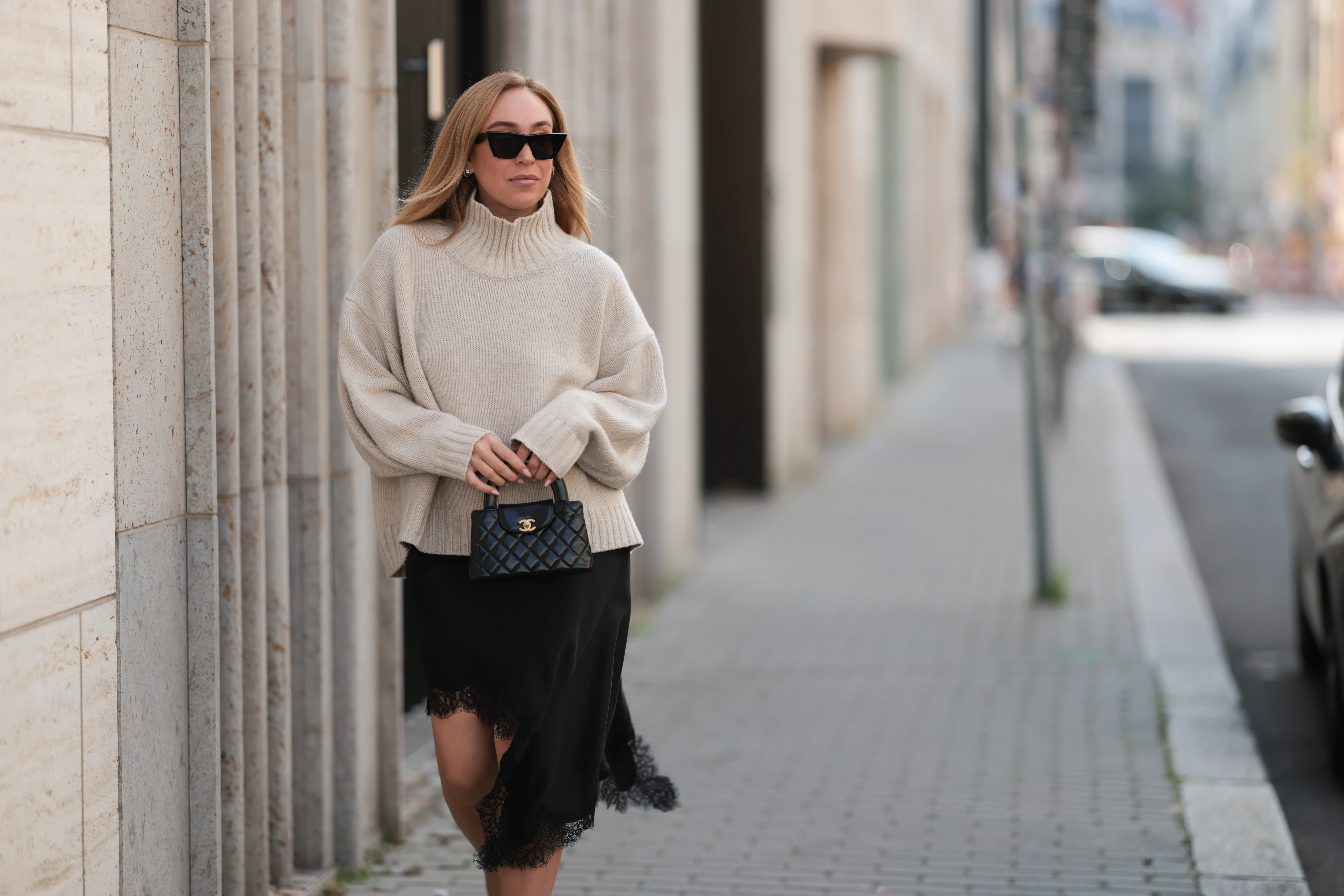 BERLIN, GERMANY - AUGUST 20: Sonia Lyson seen wearing Celine black cat-eye sunglasses, COS relaxed oversized beige turtleneck sweater in a chunky knit with dropped shoulders, Zara black asymmetrical slip dress featuring delicate lace trim along the hem and Chanel small black quilted top-handle Kelly bag with gold CC logo hardware, on August 20, 2025 in Berlin, Germany. (Photo by Jeremy Moeller/Getty Images)