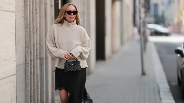 BERLIN, GERMANY - AUGUST 20: Sonia Lyson seen wearing Celine black cat-eye sunglasses, COS relaxed oversized beige turtleneck sweater in a chunky knit with dropped shoulders, Zara black asymmetrical slip dress featuring delicate lace trim along the hem and Chanel small black quilted top-handle Kelly bag with gold CC logo hardware, on August 20, 2025 in Berlin, Germany. (Photo by Jeremy Moeller/Getty Images)