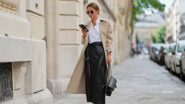 PARIS, FRANCE - SEPTEMBER 05: Diane Batoukina wears round sunglasses by Montblanc, a beige trench coat by Oak & Fort, a white shirt / blouse by Max Mara, a black quilted leather Chanel bag, a slit leather skirt by l'Agence Fashion, black shoes, holds a mobile phone / smartphone, during a street style fashion photo session, on September 05, 2025 in Paris, France. (Photo by Edward Berthelot/Getty Images)