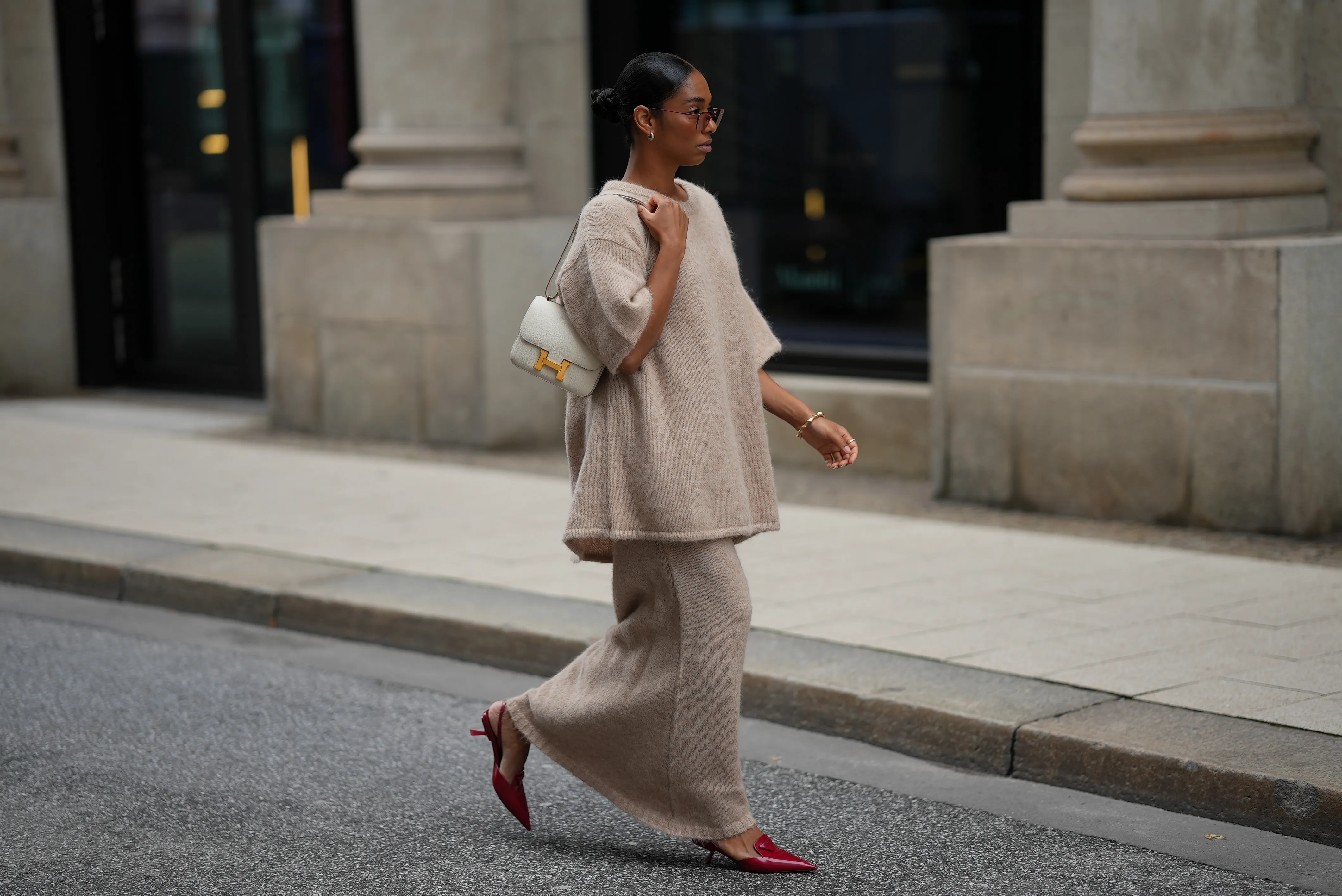HAMBURG, GERMANY - SEPTEMBER 19: Cherifa Akili is seen wearing an oversized beige short-sleeve knit sweater with a soft texture from Byaylinkönig; a matching long knit skirt in a beige tone with subtle seaming at the hem from Byaylinkönig; red pointed-toe heels with a low cut from Prada; The Constance structured white leather shoulder bag with a gold clasp from Hermes; a gold spiral shaped bracelet from Elouise; two gold, metallic rings from Elouise, Wempe; lightly tinted sunglasses in a warm shade COS; her black hair is pulled back in a sleek bun on September 19, 2025 in Hamburg, Germany. (Photo by Moritz Scholz/Getty Images)