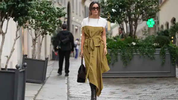 MILAN, ITALY - SEPTEMBER 27: Tamara Kalinic wears long dark brown hair styled in a low loose ponytail with a center part, black rectangular sunglasses, a gold choker-length necklace with matching gold bracelet and rings, a brown suede top-handle satchel bag, a mustard yellow patterned midi dress with a white shoulder yoke and capped sleeves, a self-tie waist belt and an asymmetrical handkerchief hem in a lightweight woven fabric, dark brown leather knee-high boots with a stacked high heel, outside Ferragamo, during Milan Fashion Week - Womenswear Spring/Summer 2026, on September 27, 2025 in Milan, Italy (Photo by Edward Berthelot/Getty Images)
