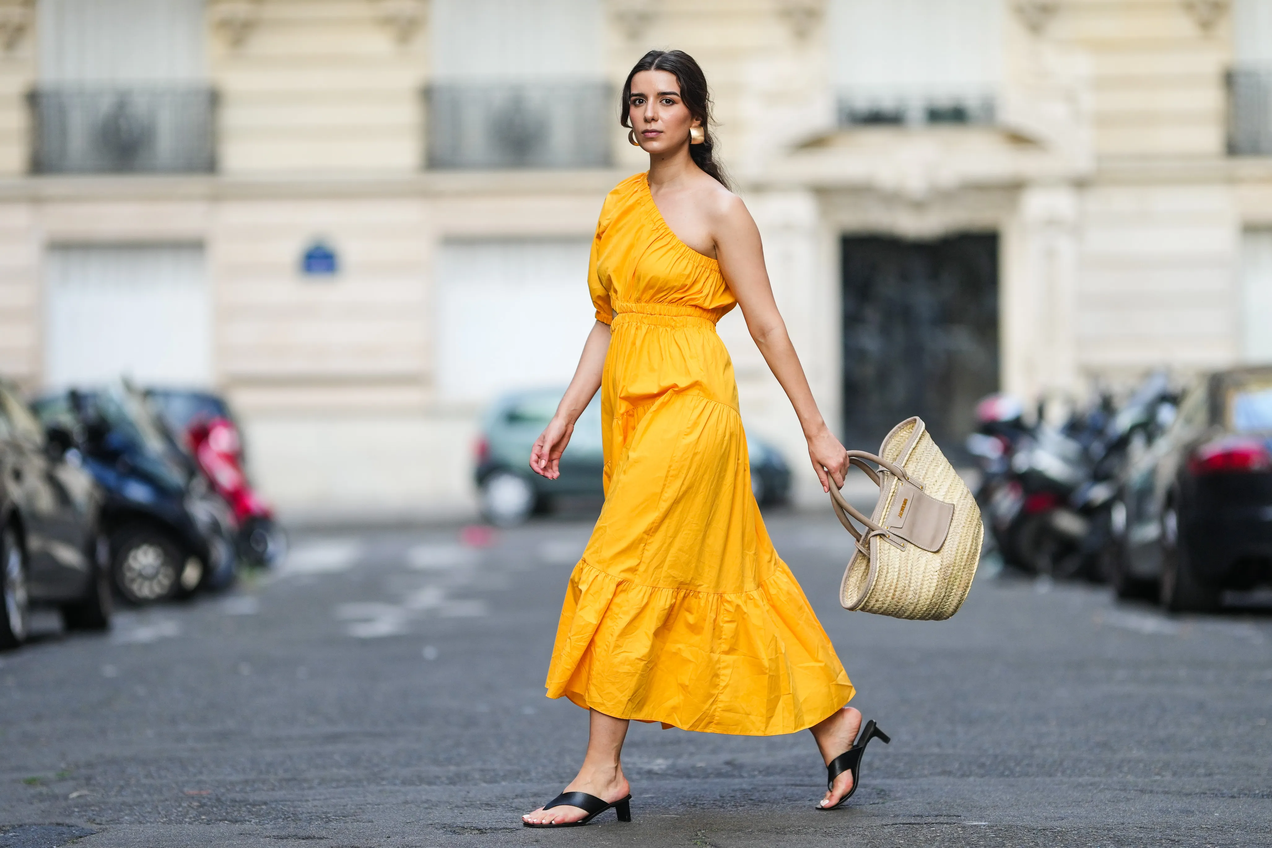 PARIS, FRANCE - AUGUST 12: Ketevan Giorgadze @katie.one wears a one shoulder cut out maxi dress in orange from Mango, oversized golden hoop earrings from Zara, flip flop heeled black sandals shoes from APC Paris, a Le Grand Panier beach straw bag by Jacquemus, on August 12, 2021 in Paris, France. (Photo by Edward Berthelot/Getty Images)