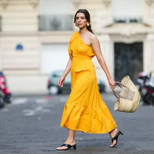 PARIS, FRANCE - AUGUST 12: Ketevan Giorgadze @katie.one wears a one shoulder cut out maxi dress in orange from Mango, oversized golden hoop earrings from Zara, flip flop heeled black sandals shoes from APC Paris, a Le Grand Panier beach straw bag by Jacquemus, on August 12, 2021 in Paris, France. (Photo by Edward Berthelot/Getty Images)