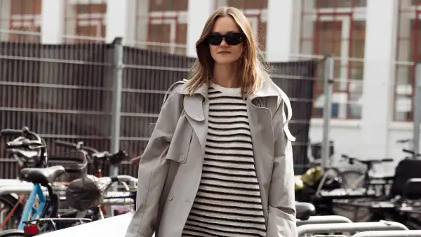 COPENHAGEN, DENMARK - AUGUST 04: A guest wears black and white stripped min dress, long black boots and grey trench coat outside Bonnetje show during Copenhagen Fashion Week day one on August 04, 2025 in Copenhagen, Denmark. (Photo by Raimonda Kulikauskiene/Getty Images)