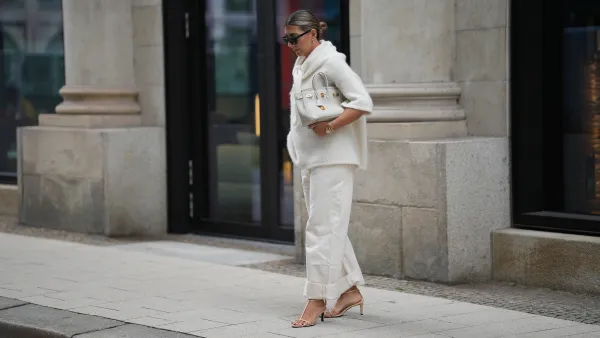 HAMBURG, GERMANY - SEPTEMBER 19: Aylin König is seen wearing a short-sleeved, fluffy textured, oversized sweater in off-white with a high, tied neckline; relaxed off-white jeans with a wide cuff at the hem; nude strappy heeled sandals; a medium-sized white leather handbag with gold hardware; black rectangular sunglasses; gold link earrings from Tiffany & Co HardWear Collection; detailed gold bracelets from Cartier; a watch with a metallic wristband and white clock face from Cartier; her dark hair is pulled back into a neat, low bun on September 19, 2025 in Hamburg, Germany. (Photo by Moritz Scholz/Getty Images)